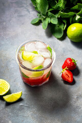 cold detox water with lime, strawberry, mint in the glass with ice cubes on gray background
