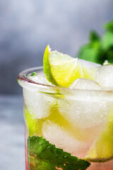 cold detox water with lime, strawberry, mint in the glass with ice cubes on gray background. close up