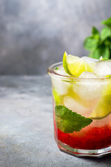cold detox water with lime, strawberry, mint in the glass with ice cubes on gray background. close up