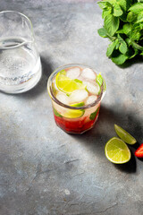 cold detox water with lime, strawberry, mint in the glass with ice cubes on gray background