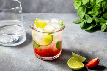 cold detox water with lime, strawberry, mint in the glass with ice cubes on gray background