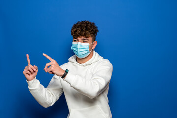Man with sterile face mask posing isolated on blue background studio portrait. Epidemic pandemic...