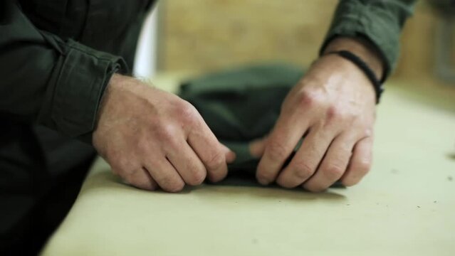 male seamstress's hands straighten the cuffs on the green trousers of a military uniform. clothing production. ironing pants. pants cuffs on the table in the room in the workshop. close-up
