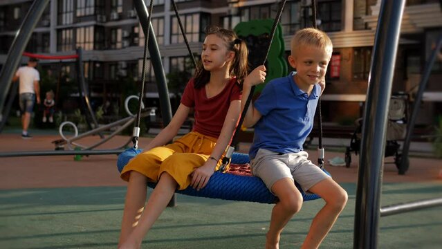 Two happy smiling children are swinging on a children's round swing on the playground.
