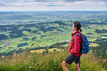Naklejka premium nice senior woman hiking at Mount Gruenten in the Allgaeu Alps with awesomw view over Iller valley to Lake Alpsee and Lake of Constanz, Bodensee, Bavaria, Germany