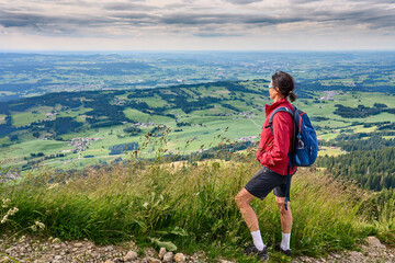 Naklejka na ściany i meble nice senior woman hiking at Mount Gruenten in the Allgaeu Alps with awesomw view over Iller valley to Lake Alpsee and Lake of Constanz, Bodensee, Bavaria, Germany