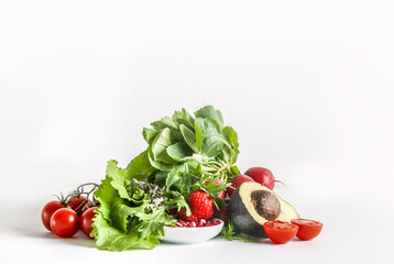 Heap of healthy salad ingredients at white background: lettuce, tomato, avocado, pomegranate seeds and raspberry. Front view.