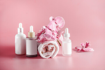 Obraz na płótnie Canvas Beauty settings with various cosmetic bottles with empty label mock up, towel and orchid flowers at pink background. Products for skin care routine. Front view with copy space.