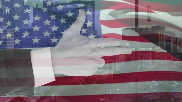 Animation of hand of smart caucasian making gun gesture over waving american flag and city buildings
