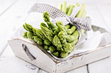 Fresh raw green asparagus bundle offered as close-up on white wooden tray