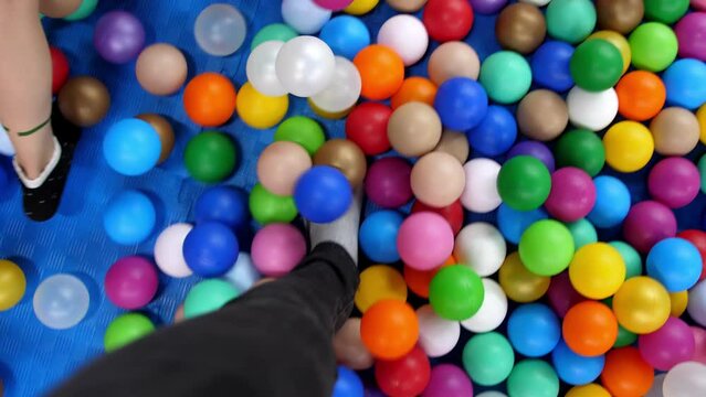 Legs in jeans and socks walk among many colorful plastic balls POV. Walking around the pool with small balls different colors, top view. father plays with children in an amusement center, playground