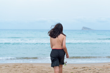 Boy with long hair goes for a swim at the Poniente beach in Benidorm wearing shorts and diving goggles.