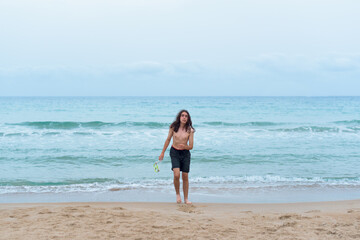 Very long shot of a teenager coming out of the sea in summer after a swim.
