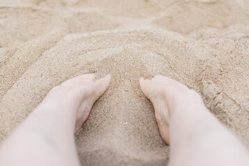 Top view and close-up of a woman's feet burying themselves in the sand on the beach.