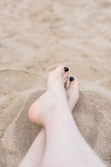 Top view and close-up of a woman's feet with black painted toenails on the sand on the beach.