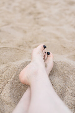 Top view and close-up of a woman's feet with black painted toenails on the sand on the beach.
