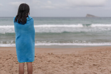 Teenager with long hair wrapped in a towel to dry himself on the beach in Benidorm