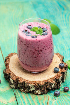 Bilberry smoothie yogurt, fresh blueberries in glass with mint leaf and raw beeries on blue background. Restaurant menu, dieting, cookbook recipe top view