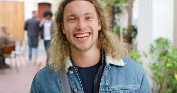 Portrait of trendy tourist happy and excited to explore the city against an urban background. Smiling handsome man and student with curly blonde hair looking cheerful and fashionable, enjoying life