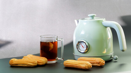 A fashionable, vintage-style electric kettle with a thermometer stands next to a mug of poured tea, with a tea bag and cakes. Copy space. Selective focus.