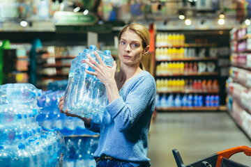 Portrait of scared woman shopper in supermarket buying water in plastic bottles and looking scared...