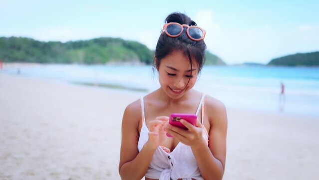 Portrait of happy smiling beautiful women using a mobile phone on the beach. Pretty young Asian girl in casual looking clothes posting a picture online outdoors