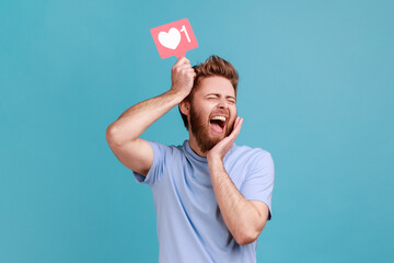 Portrait of excited bearded man holding like counter button, smiling with pleasure, rejoicing and...