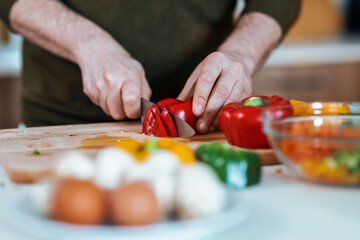 Handsome mature man cutting fresh vegetables while listening music with headphones in the kitchen at home.