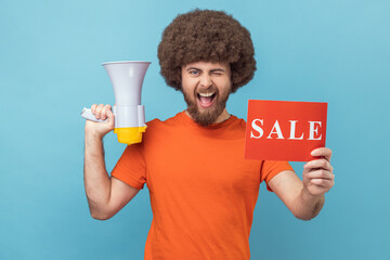 Portrait of funny man with Afro hairstyle wearing orange T-shirt holding card with sale inscription...