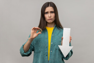 Portrait of young adult unhappy woman showing downgrade of bitcoin, expressing sad upset emotions,...