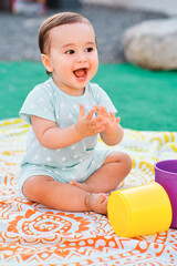 One year old baby playing with colored cubes sitting on a blanket in the garden of his house.