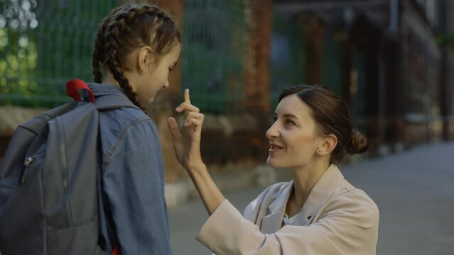 Mother gives advices to her schoolchild on the street before school time. Adult female points finger on nose close up