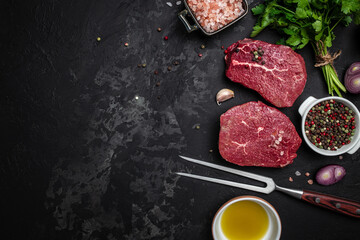 Two fresh raw beef steaks with spices ready to cook on a dark background. Culinary, cooking, concept. banner, menu, recipe place for text, top view
