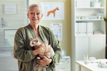 Waist up portrait of smiling senior woman holding hairless cat in vet clinic at pet health check...