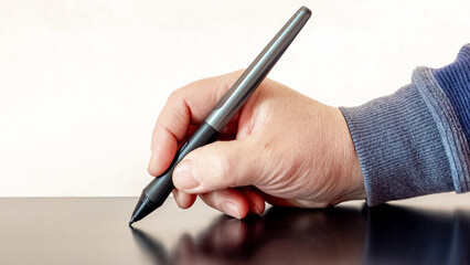 A man holds a pen, a stylus and draws with a graphics tablet