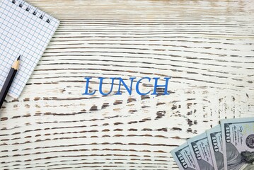 Naklejka premium LUNCH - word (text) and dollars on a white wooden table, notebook, notepad. Business concept: buying, selling, commerce (copy space).