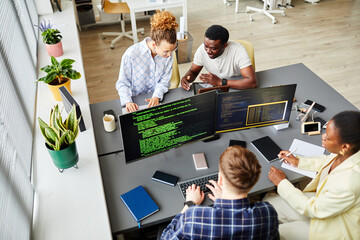High angle view of programmers sitting at table with computer monitors and writing codes in team at office