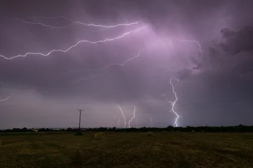Fotobehang Thunderstorm above field with roll bales of hay at night, cloud to ground branched lightning, lightning in clouds at night in countryside © slobodan