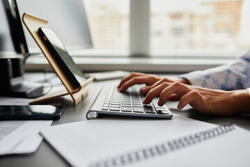 Close-up of young programmer typing on keyboard to write code of software while sitting in front of digital tablet at table