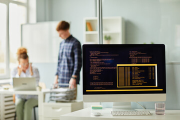 Close-up of computer codes of new software on monitor standing on office desk with programmers working in background