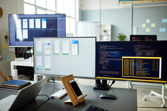Horizontal image of computer monitors with programs and computer codes on monitors standing on workplace of programmer