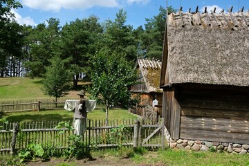 Fototapeta na wymiar Scarecrow in a garden in the countryside by a wooden fence and cottages. Wdzydze Kiszewskie, Kashubia, Poland