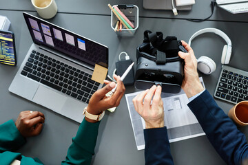 High angle view of programmers testing new virtual reality glasses at table using laptop and smartphone