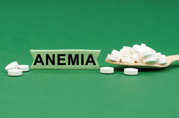 On a green surface, a wooden spoon with pills and a sign with the inscription - ANEMIA