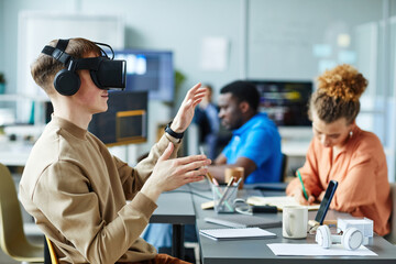 Young man in virtual reality glasses sitting at meeting with colleagues and testing new VR application