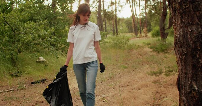 Woman volunteer with trash bag in hands cleaning forest from garbage. Ecology problems
