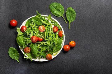 Fresh juicy salad with arugula, baby spinach and cherry tomatoes on dark rustic table top view....