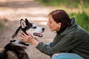 adult woman hugs her furry friend siberian husky on the background of a forest road.