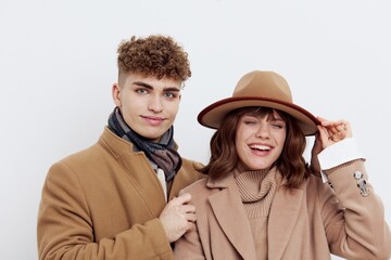 a sweet, loving couple stands on a white background in autumn clothes and the guy adjusts the hat on the head of a joyful woman looking at the camera