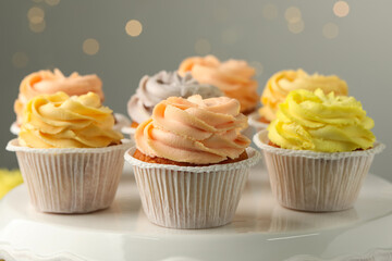 Tasty cupcakes on white stand against blurred lights, closeup